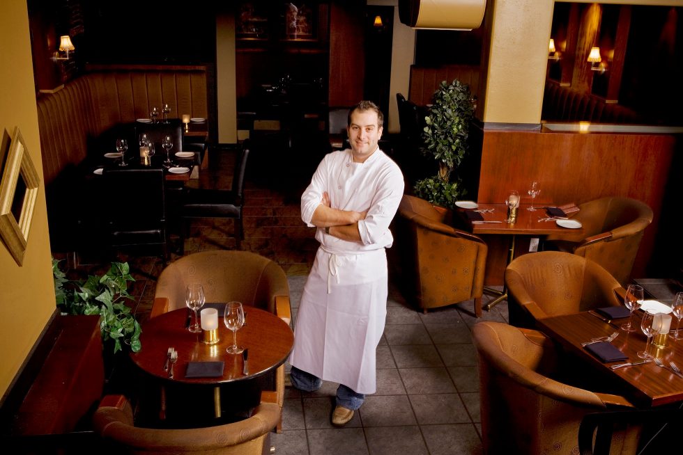 Calgary People Photographer. Chef standing in dining area with arms crossed.